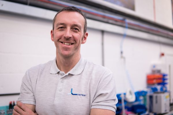 A smiling man in a workshop wearing a t-shirt with the Lontra logo